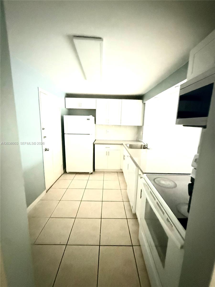 A galley-style kitchen features white cabinets, white appliances, and light-colored tile flooring — 9611 SW 77th Ave # 108A, Miami FL 33156, MIAMI, FL
