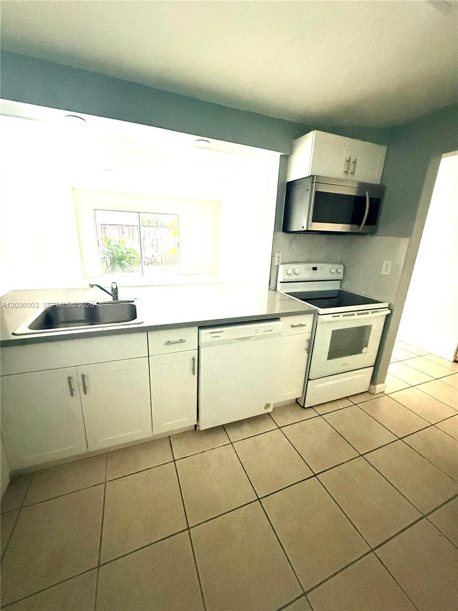 A kitchen features white cabinets, a stainless steel sink, a dishwasher, and a white stove — 9611 SW 77th Ave # 108A, Miami FL 33156, MIAMI, FL