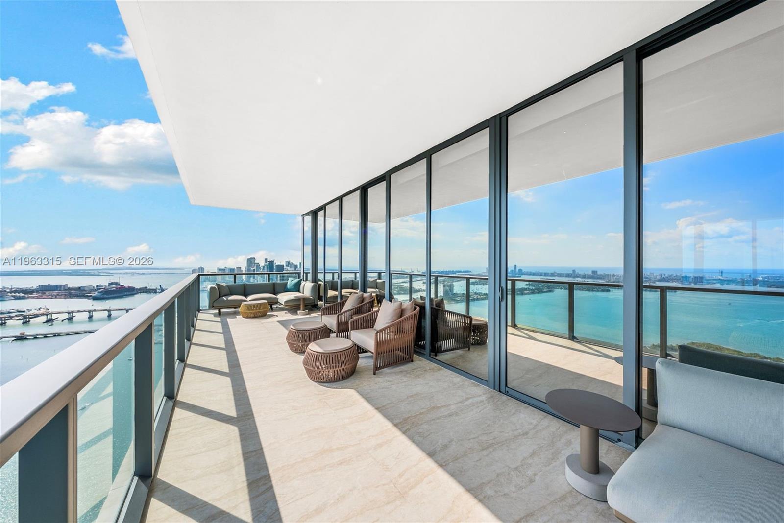 A spacious high-rise balcony features outdoor furniture, glass railings, and panoramic water and city views — 788 NE 23rd St # 5501, Miami FL 33137, MIAMI, FL