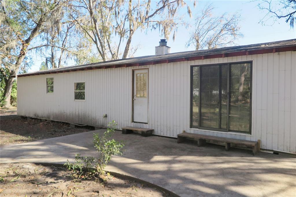 A single-story house with white vertical siding, a concrete patio, and a sliding glass door — 8760 COUNTY ROAD 127, SANDERSON, FL