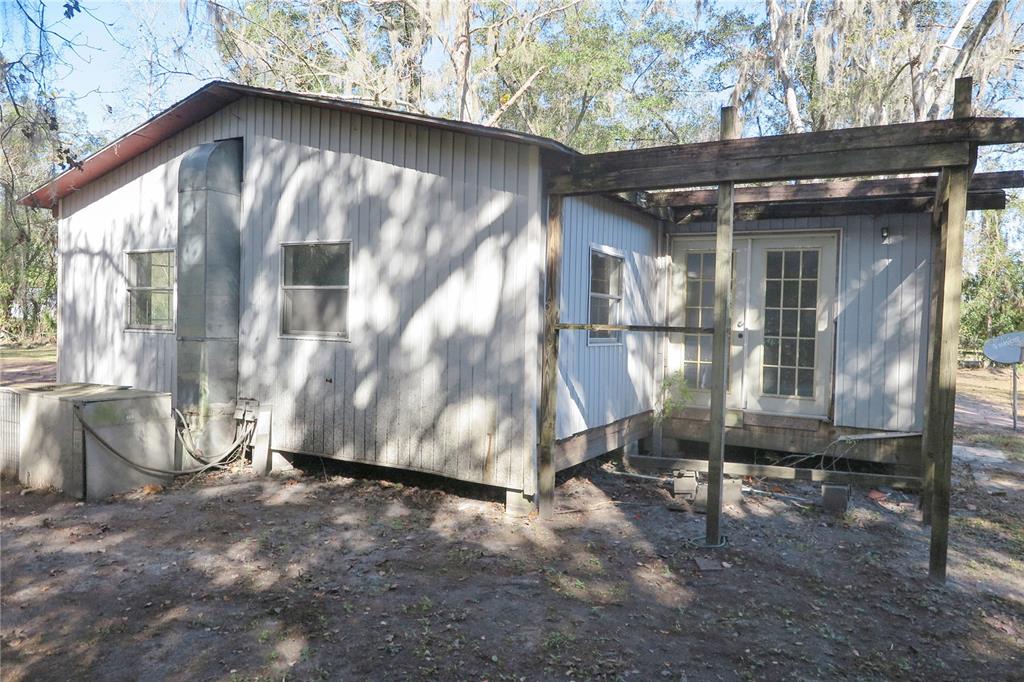 The exterior of a weathered, light-colored house with a wooden pergola over the back entrance — 8760 COUNTY ROAD 127, SANDERSON, FL