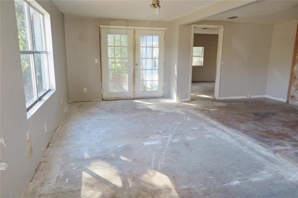 An unfinished room with bare concrete floors, white walls, and French doors leading outside — 8760 COUNTY ROAD 127, SANDERSON, FL