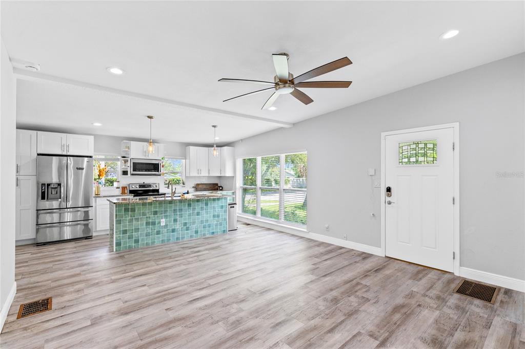 An open-concept kitchen and living area featuring wood-look flooring, a teal tiled island, and white cabinetry — 1502 MONTCALM STREET, ORLANDO, FL
