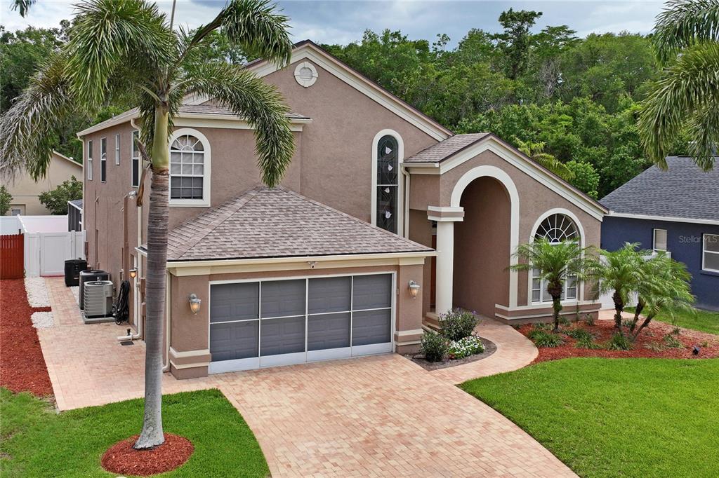 A two-story tan stucco house with a paved driveway, arched entryway, and a palm tree — 277 WOOD DOVE AVENUE, TARPON SPRINGS, FL