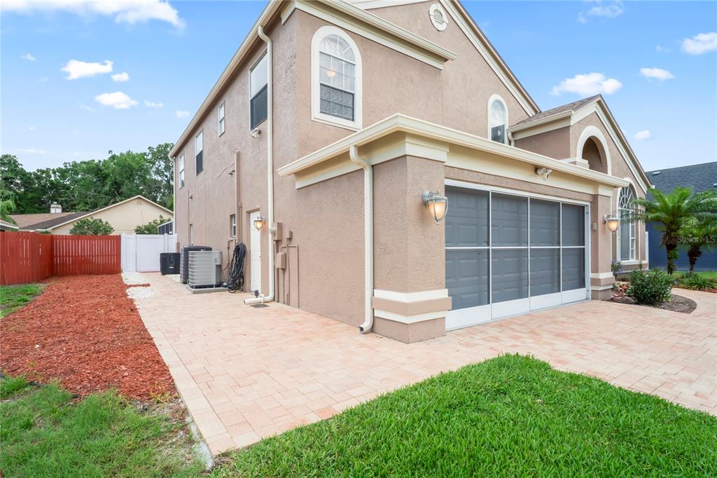 A tan two-story house exterior with a paved patio and a screened-in garage area — 277 WOOD DOVE AVENUE, TARPON SPRINGS, FL