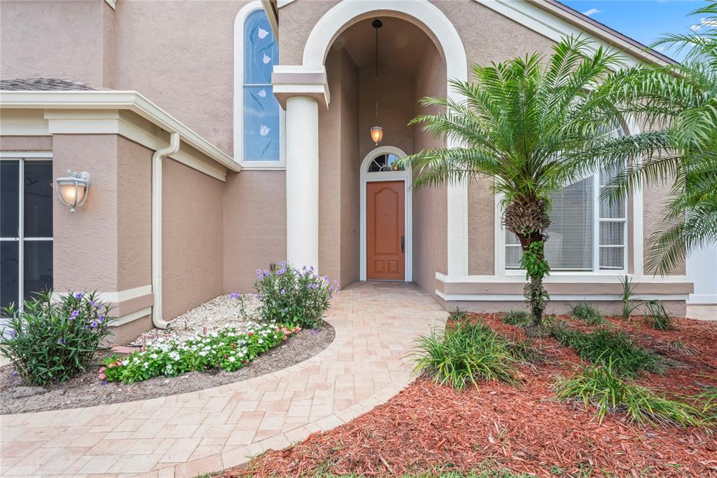 The exterior of a house features a tan stucco facade, arched entryway, and paved walkway — 277 WOOD DOVE AVENUE, TARPON SPRINGS, FL
