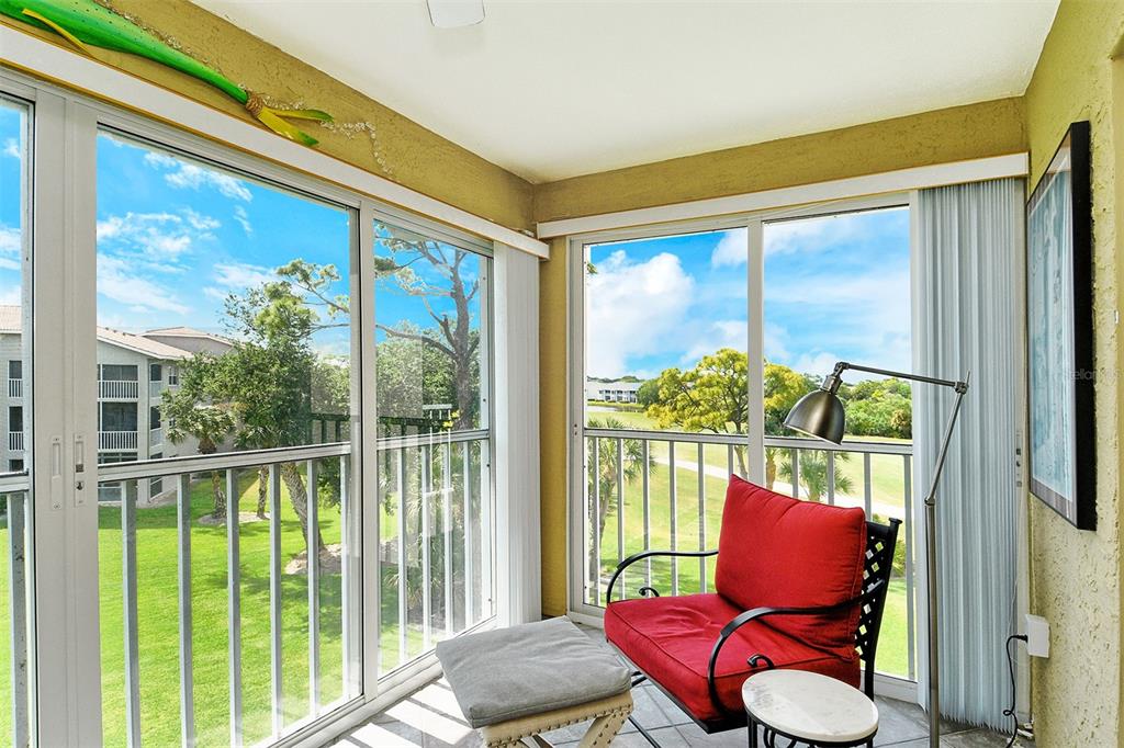 A sunroom with tile floors, a red armchair, and large windows overlooking a grassy area — 9610 CLUB SOUTH CIRCLE UNIT 4302, SARASOTA, FL