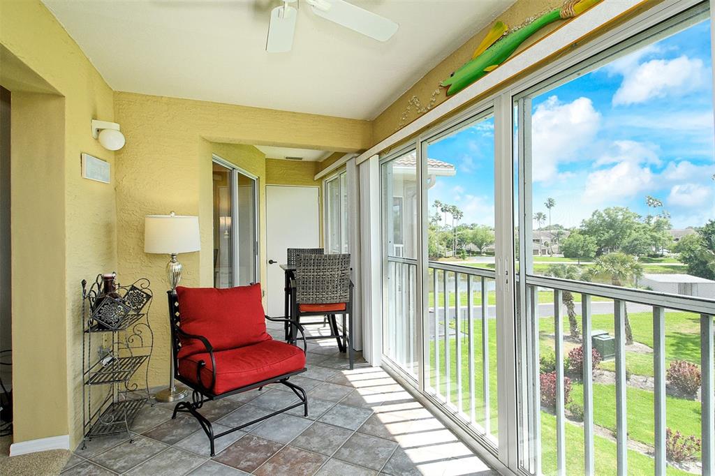 A sunroom with tile flooring, a red armchair, and sliding glass doors overlooking a grassy area — 9610 CLUB SOUTH CIRCLE UNIT 4302, SARASOTA, FL