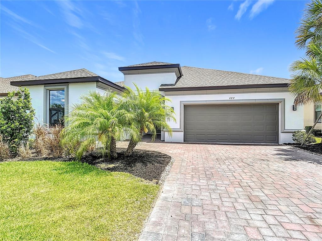 A single-story house exterior features a gray garage, a paver driveway, and a palm tree — 684 SAN AUGUSTO DRIVE, POINCIANA, FL