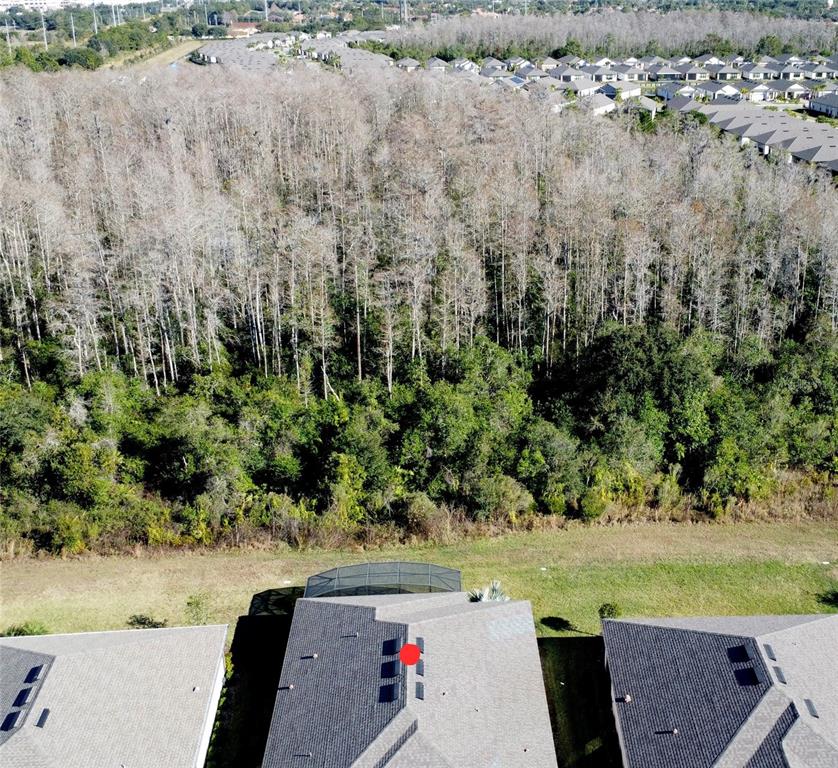 An aerial view shows a residential house with solar panels on the roof near woods — 684 SAN AUGUSTO DRIVE, POINCIANA, FL