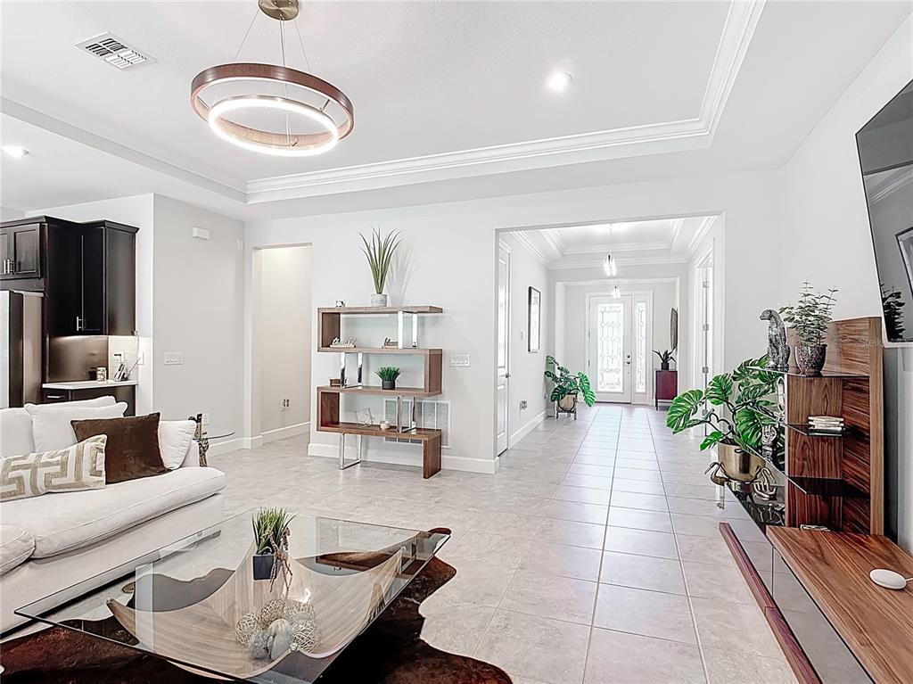 A living room features tile floors, a modern chandelier, and an open entryway — 684 SAN AUGUSTO DRIVE, POINCIANA, FL