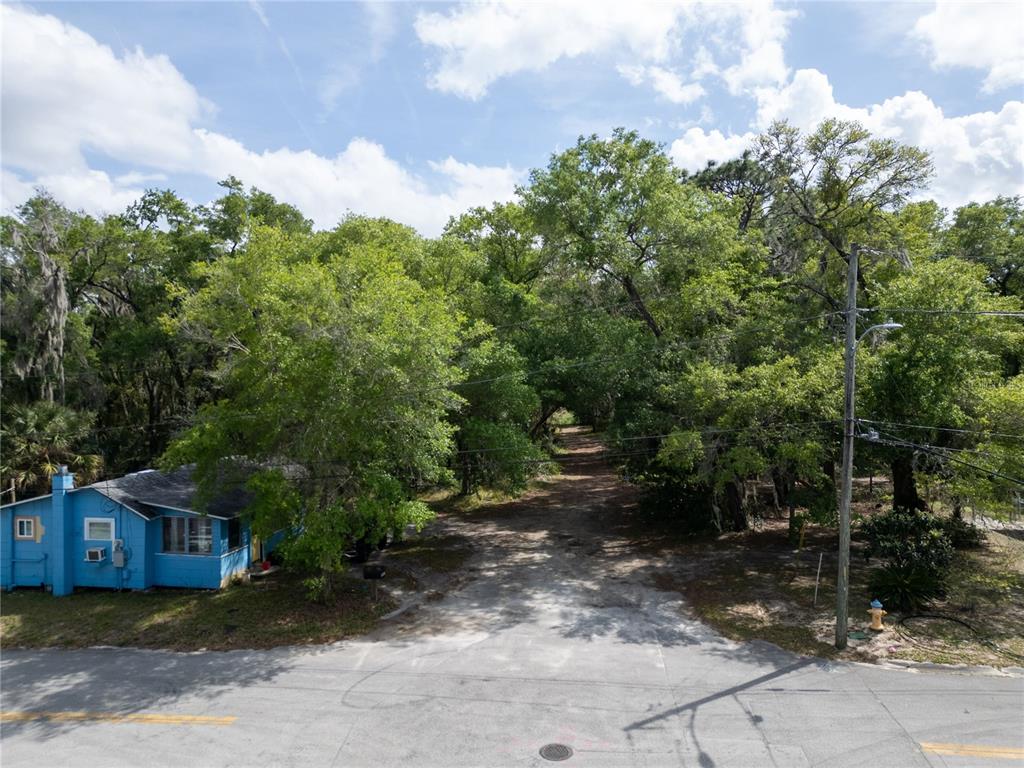 An aerial view shows a blue house next to a dirt driveway lined with trees — E HUBBARD AVENUE, DELAND, FL