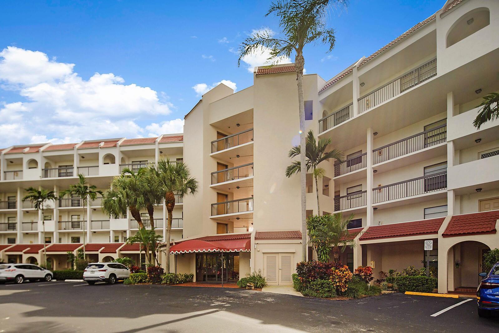 Exterior view of a multi-story apartment building with balconies, palm trees, and a parking lot — 3485 Environ Boulevard # C106, Lauderhill FL 33319, LAUDERHILL, FL