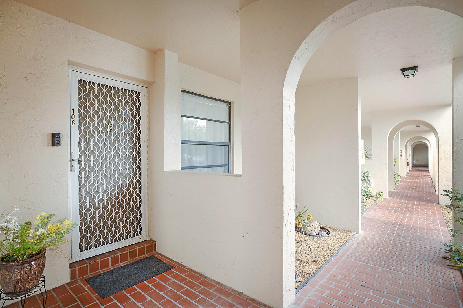 An exterior view of a covered walkway with arched openings leading to apartment unit 106 — 3485 Environ Boulevard # C106, Lauderhill FL 33319, LAUDERHILL, FL