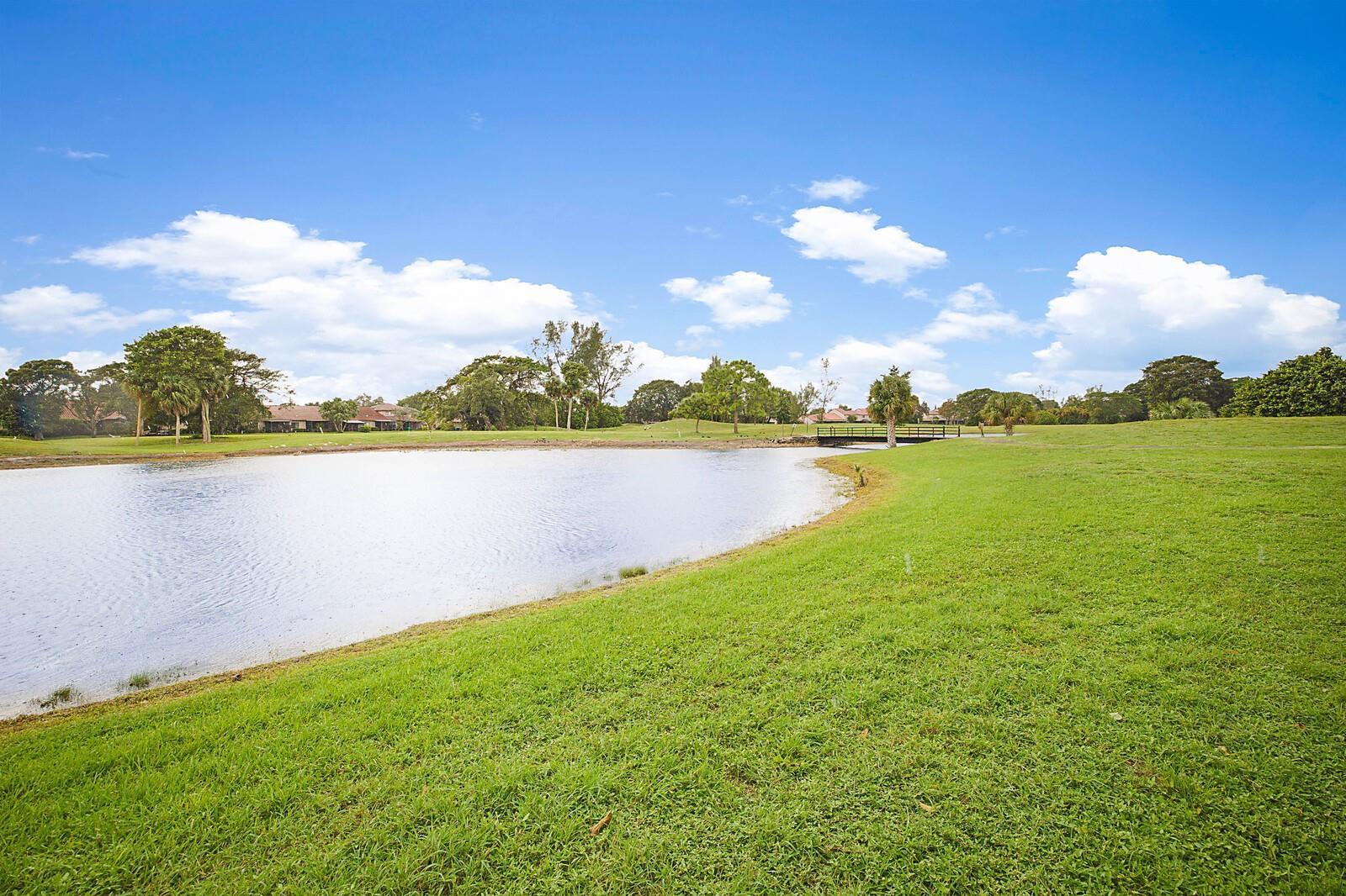 A grassy lawn slopes down to a pond on a sunny day with trees nearby — 3485 Environ Boulevard # C106, Lauderhill FL 33319, LAUDERHILL, FL