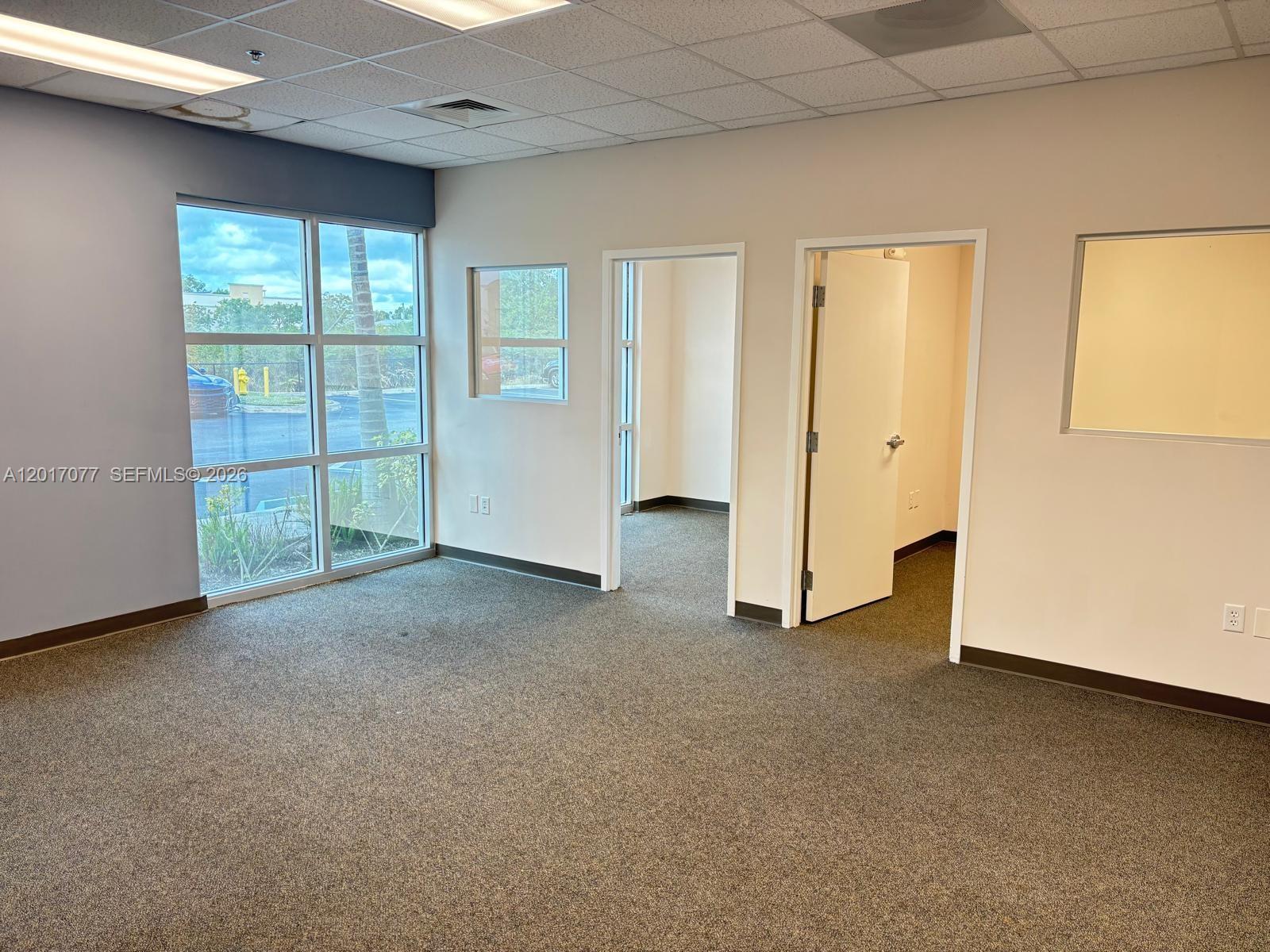 An empty office space features gray carpet, beige walls, large windows, and two interior doorways — 10380 W State Road 84, Davie FL 33324, DAVIE, FL
