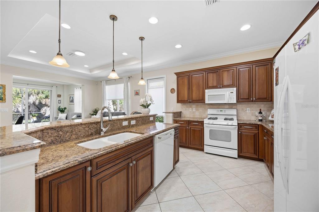 A kitchen with wood cabinets, granite countertops, white appliances, and a breakfast bar — 225 MESTRE PLACE, NORTH VENICE, FL