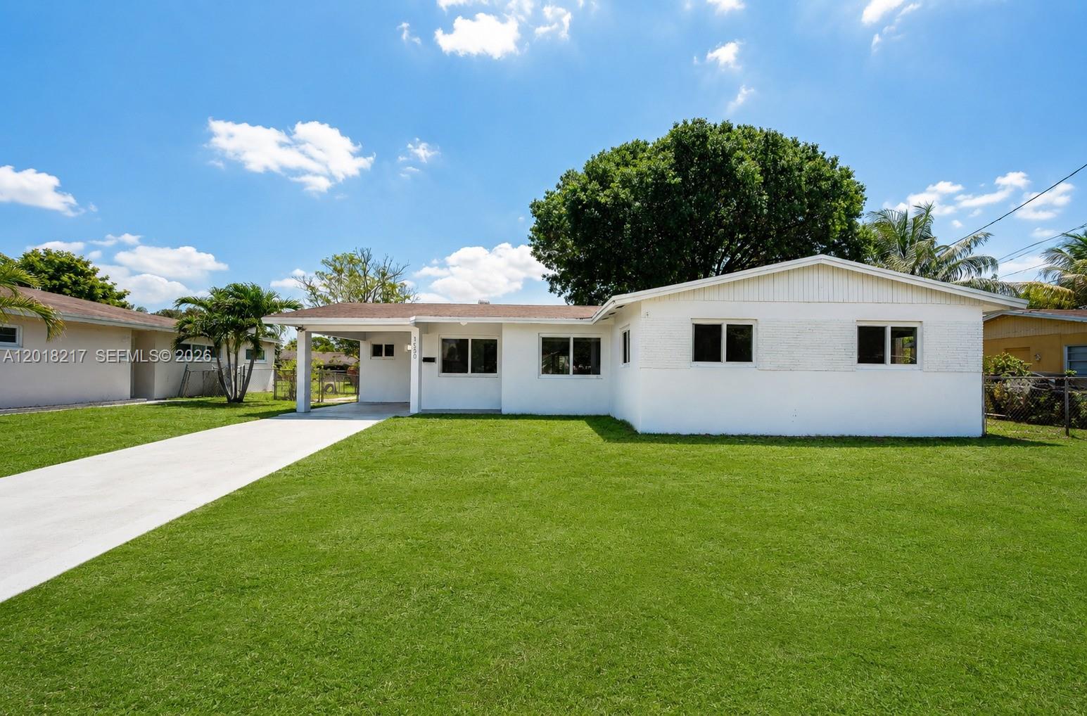 A white single-story house with a carport and a large front lawn under a blue sky — 1530 NW 47th Ave, Lauderhill FL 33313, LAUDERHILL, FL