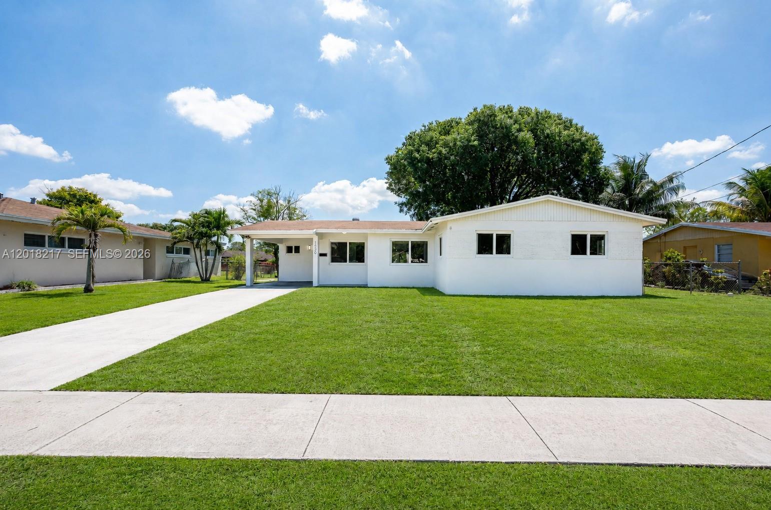 A white, single-story house with a carport and a large front lawn under a blue sky — 1530 NW 47th Ave, Lauderhill FL 33313, LAUDERHILL, FL