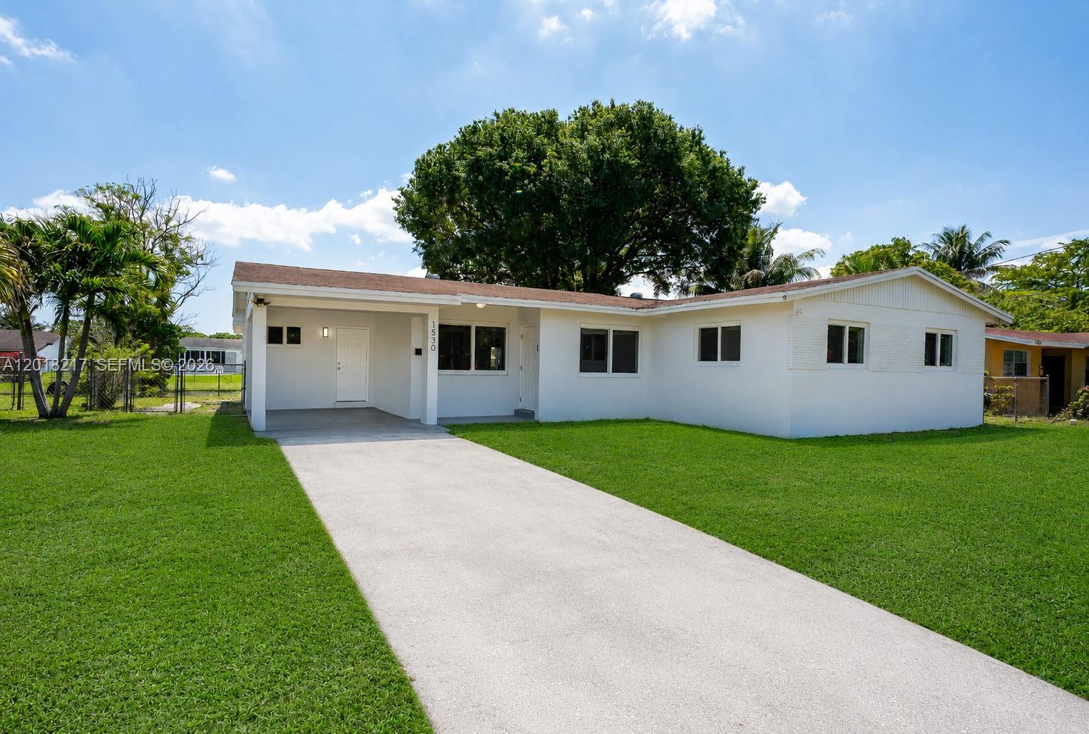 A single-story white house with a concrete driveway and a carport under a blue sky — 1530 NW 47th Ave, Lauderhill FL 33313, LAUDERHILL, FL
