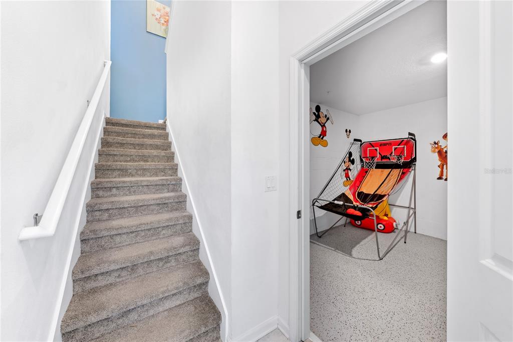 A carpeted staircase sits beside a room containing a basketball arcade game — 1069 SPLASH SHOT PLACE UNIT 1804, DAVENPORT, FL