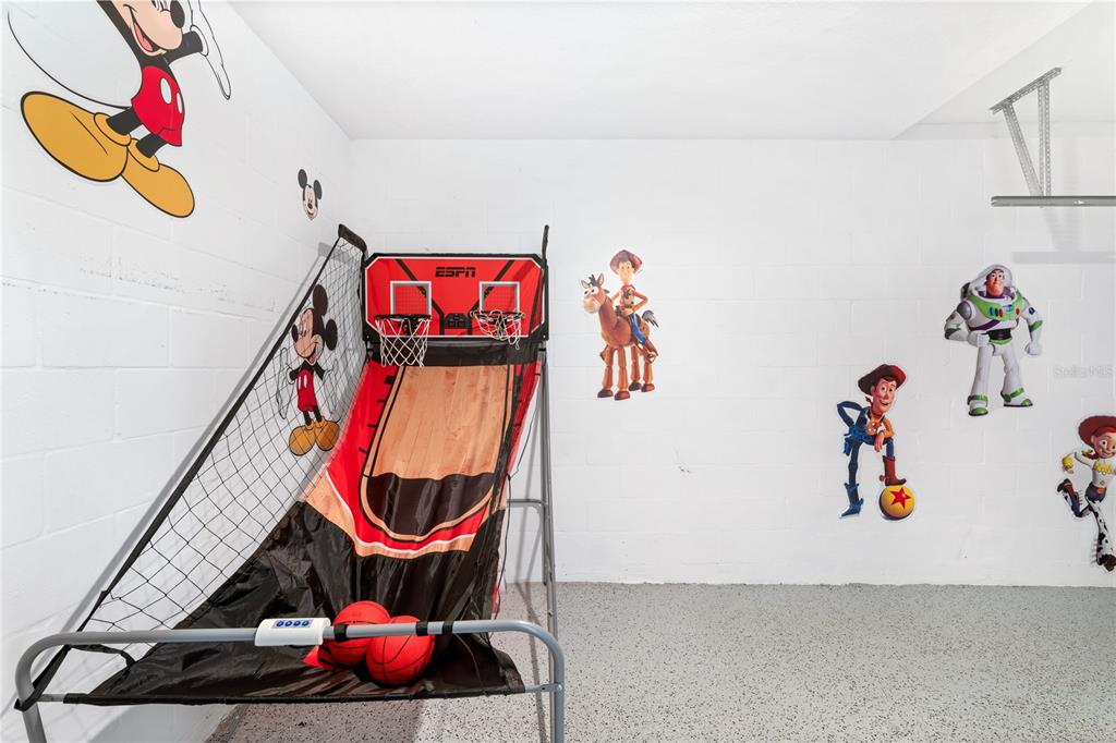 A garage playroom features a basketball arcade game and Disney character wall decals — 1069 SPLASH SHOT PLACE UNIT 1804, DAVENPORT, FL