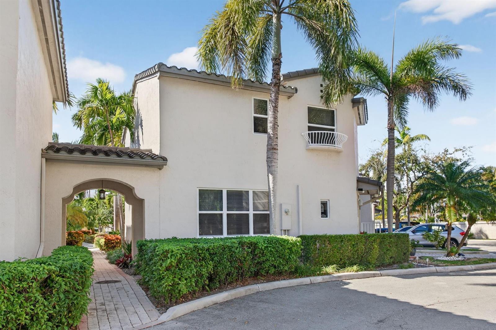 A two-story stucco building features an arched entryway, a small balcony, and palm trees — 1900 Oceanwalk Lane # 138, Pompano Beach FL 33062, POMPANO BEACH, FL