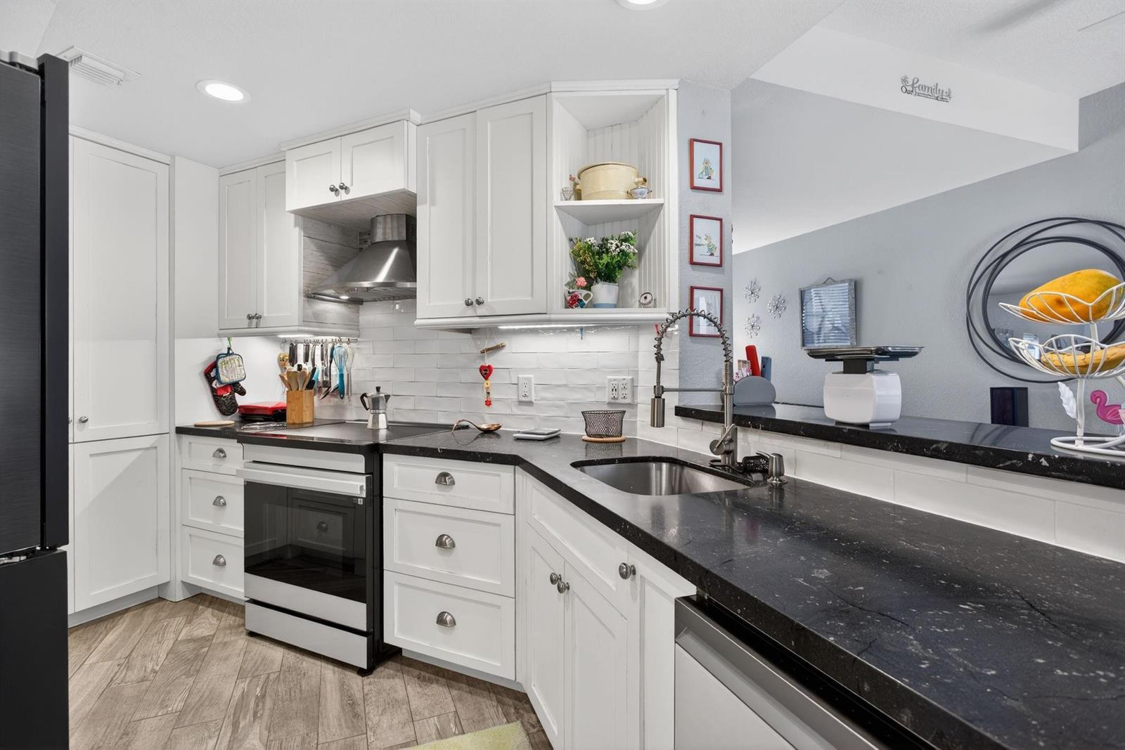A kitchen features white cabinets, black countertops, stainless steel appliances, and a subway tile backsplash — 1900 Oceanwalk Lane # 138, Pompano Beach FL 33062, POMPANO BEACH, FL