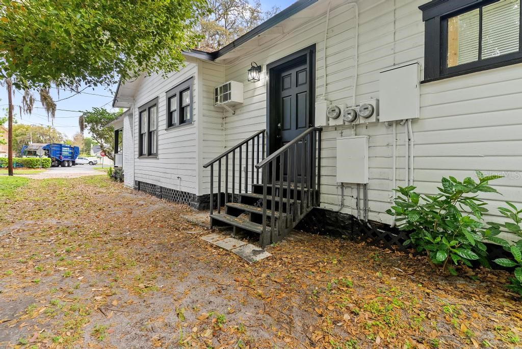A white house exterior features a black door, wooden stairs, and an air conditioning unit — 412 E HARWOOD STREET UNIT 4, ORLANDO, FL