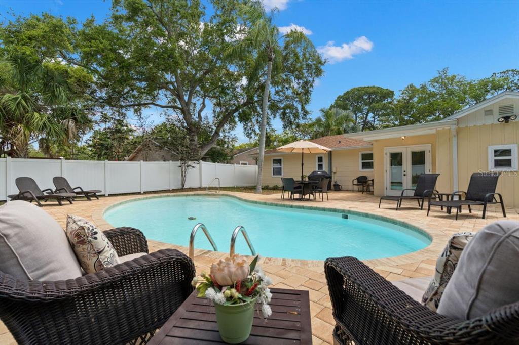 A backyard features a swimming pool, patio furniture, and a white fence under a blue sky — 1658 DOUGLAS AVENUE, DUNEDIN, FL