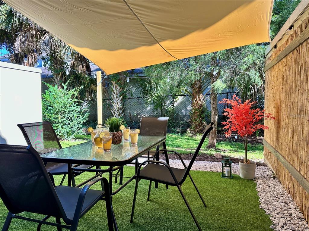 A patio with a glass-top dining table, chairs, and a shade sail on artificial turf — 8111 ROSEVILLE BOULEVARD, DAVENPORT, FL