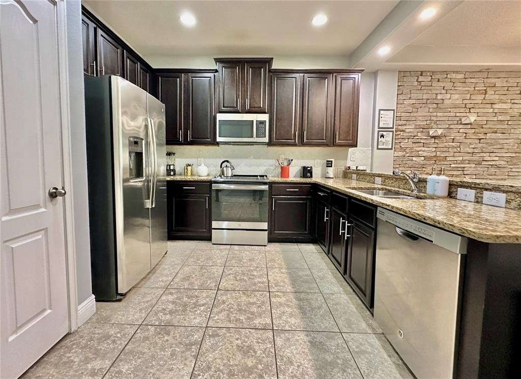 A kitchen features dark wood cabinets, stainless steel appliances, granite countertops, and tiled flooring — 8111 ROSEVILLE BOULEVARD, DAVENPORT, FL