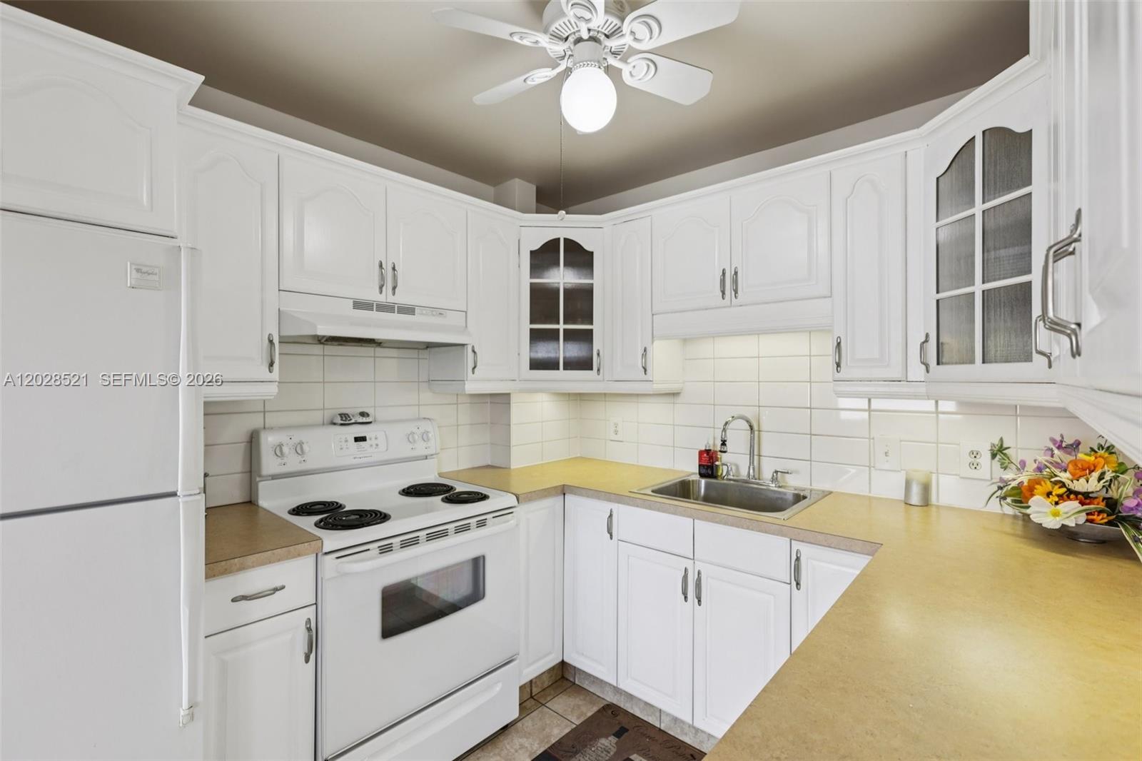 A kitchen features white cabinets, white appliances, a tan countertop, and a ceiling fan — 22 SE 3rd Ter # 18, Dania Beach FL 33004, DANIA BEACH, FL