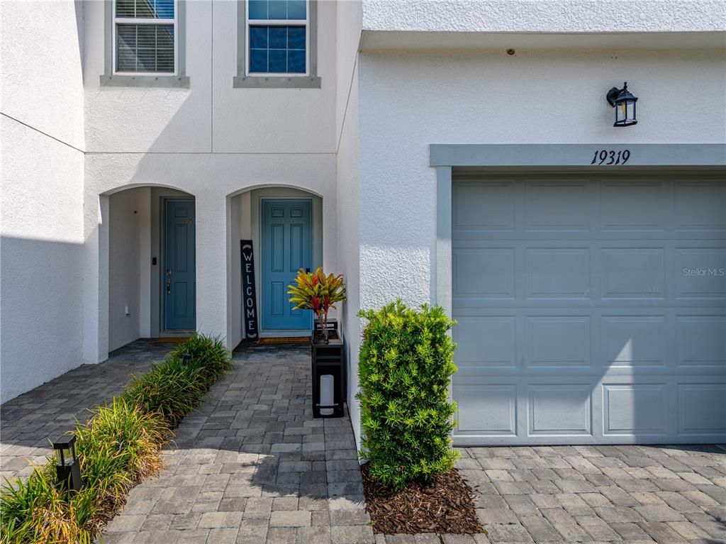 The exterior of a two-story townhouse features a gray garage, blue front doors, and pavers — 19319 BLUE POND DRIVE UNIT 22, LUTZ, FL