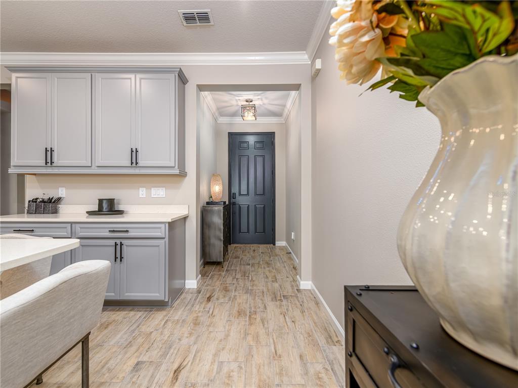 A kitchen with gray cabinets and wood-look tile flooring leads to a dark entry door — 19319 BLUE POND DRIVE UNIT 22, LUTZ, FL