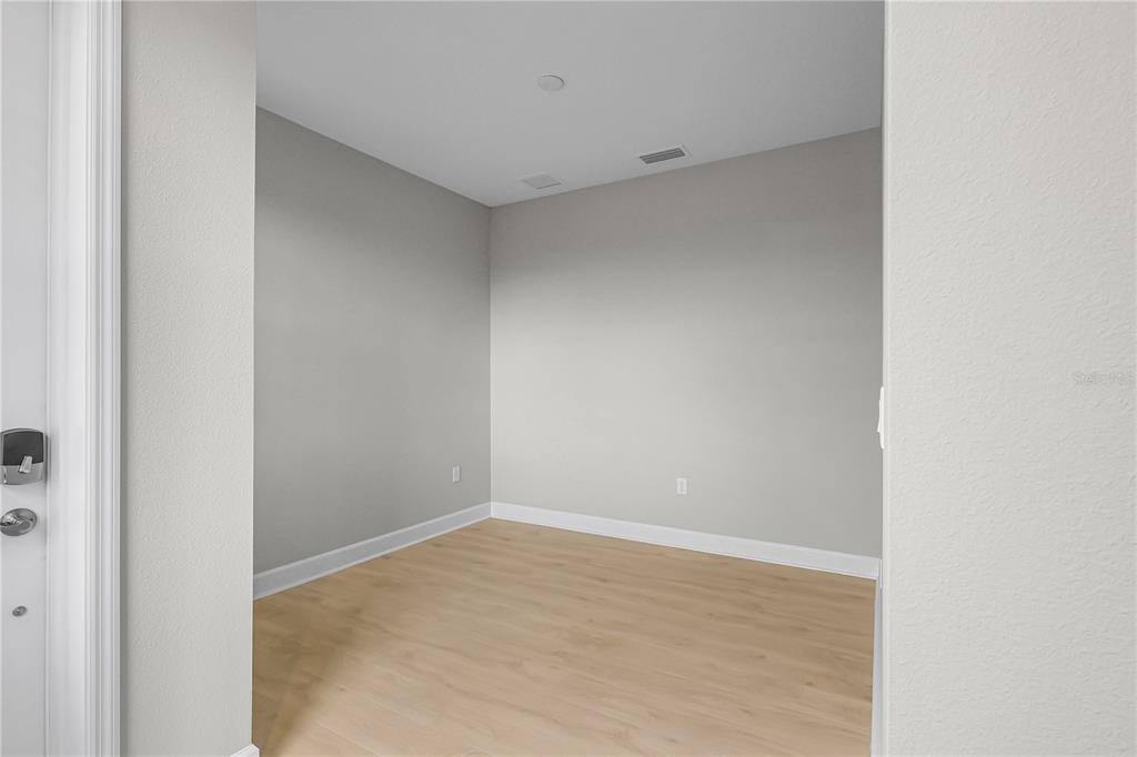 An empty room features light gray walls, light wood-look flooring, and white baseboards — 1457 SANTORINI WAY, TAVARES, FL