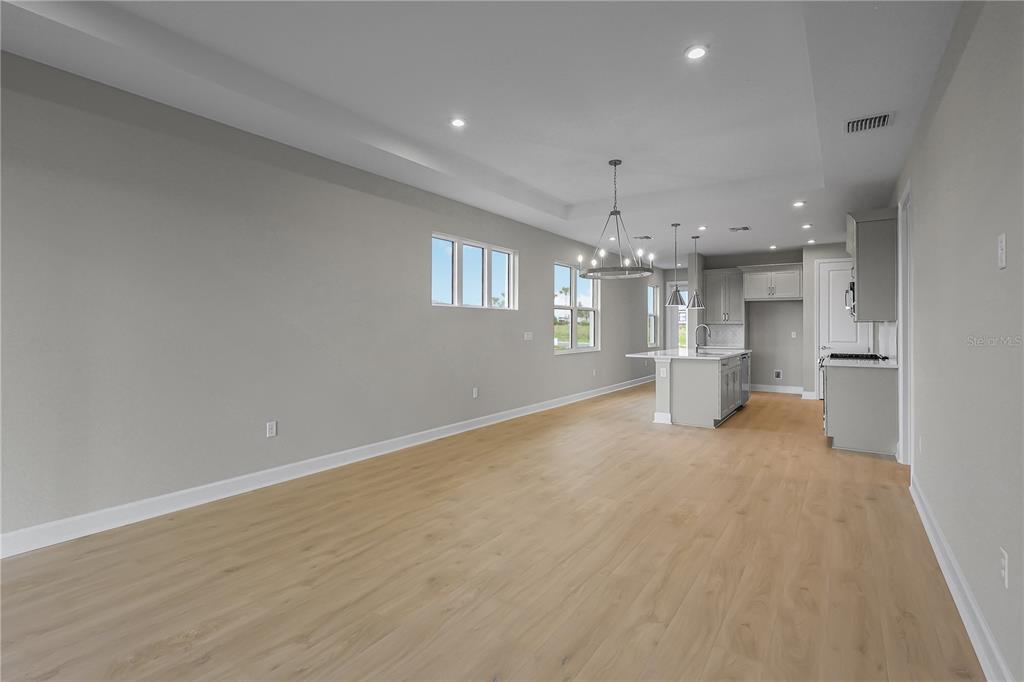 An open-concept kitchen and living area features light wood flooring, gray cabinetry, and recessed lighting — 1457 SANTORINI WAY, TAVARES, FL