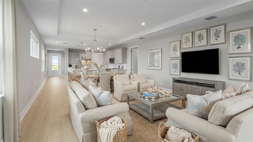 A bright, open-concept living room and kitchen featuring light wood floors and neutral furniture — 1457 SANTORINI WAY, TAVARES, FL