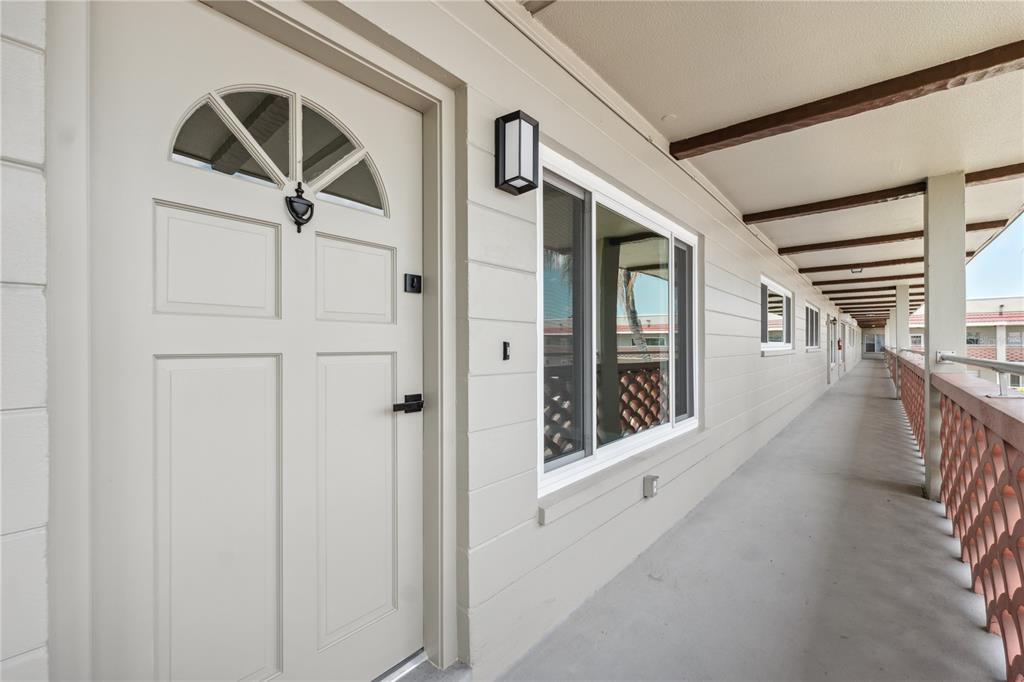 An exterior view of a building walkway featuring a white door with a glass insert — 2072 AUSTRALIA WAY W UNIT 42, CLEARWATER, FL