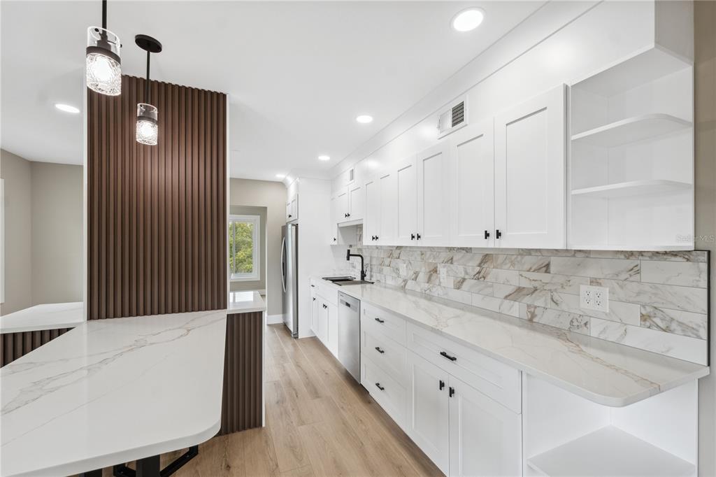 A modern kitchen features white cabinets, marble-patterned countertops, a slatted wood accent wall, and wood flooring — 2072 AUSTRALIA WAY W UNIT 42, CLEARWATER, FL