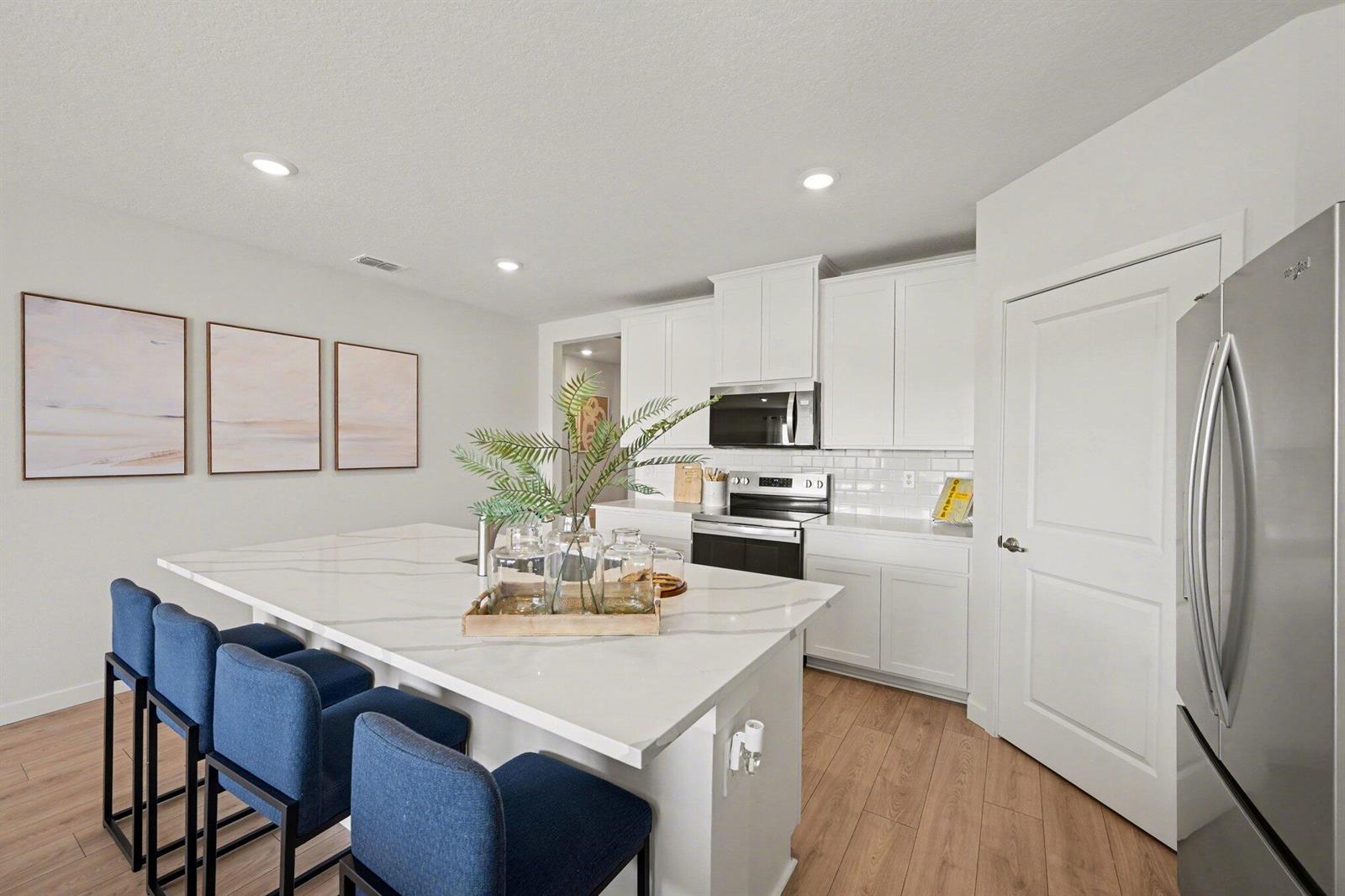 A modern kitchen features a white marble island, blue bar stools, and white cabinetry — 9069 Venetian Square, Vero Beach FL 32966, VERO BEACH, FL