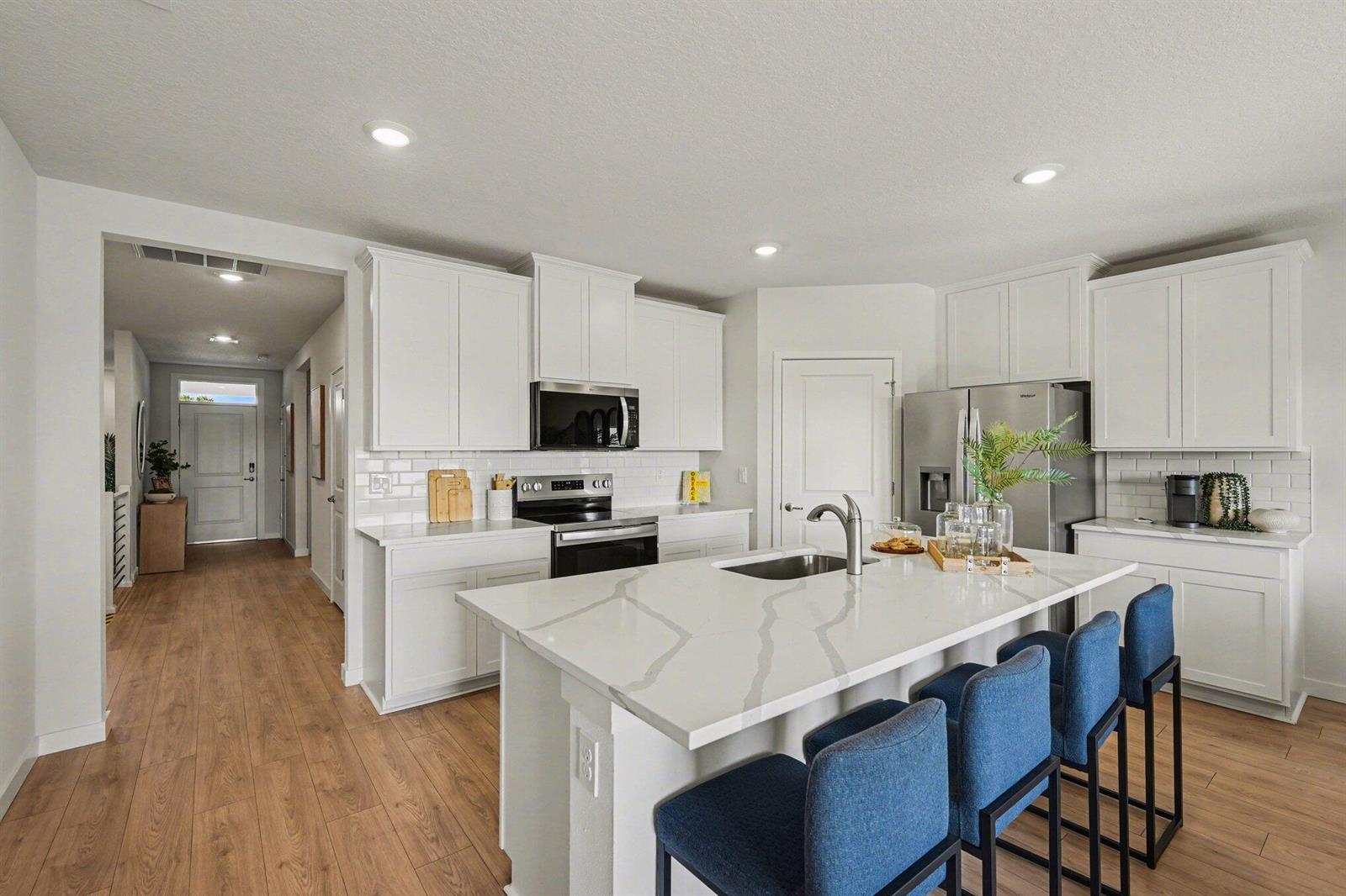 A modern kitchen features white cabinets, a quartz island with blue stools, and wood flooring — 9069 Venetian Square, Vero Beach FL 32966, VERO BEACH, FL