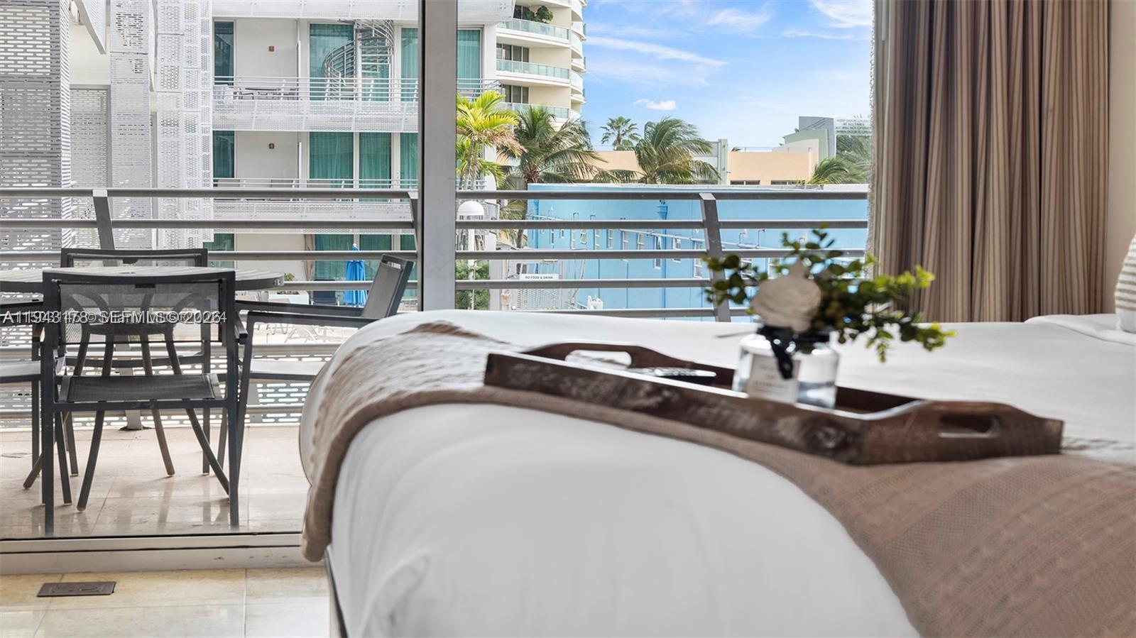 A bedroom with a wooden tray on the bed and a balcony overlooking buildings — 1437 Collins Ave # 327, Miami Beach FL 33139, MIAMI BEACH, FL