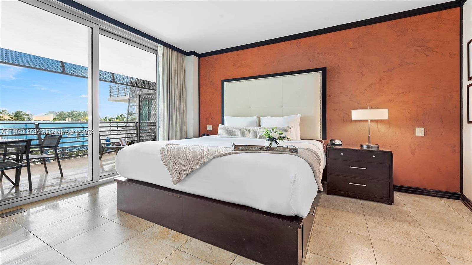A bedroom features a king bed, terracotta-colored wall, tile flooring, and a balcony with seating — 1437 Collins Ave # 327, Miami Beach FL 33139, MIAMI BEACH, FL