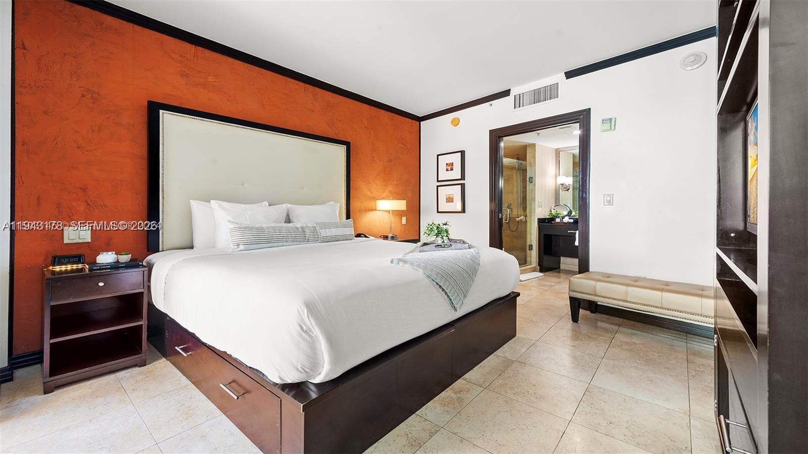 A bedroom features a king bed against an orange wall, tile flooring, and an attached bathroom — 1437 Collins Ave # 327, Miami Beach FL 33139, MIAMI BEACH, FL