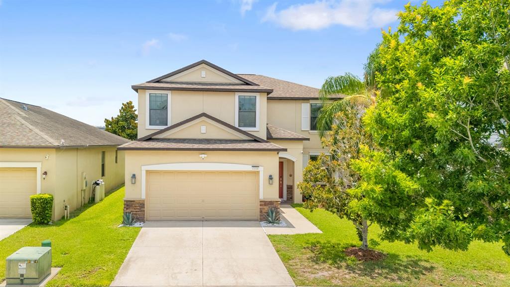 A two-story suburban house features a beige stucco exterior, a two-car garage, and a lawn — 13216 WELLINGTON HILLS DRIVE, RIVERVIEW, FL