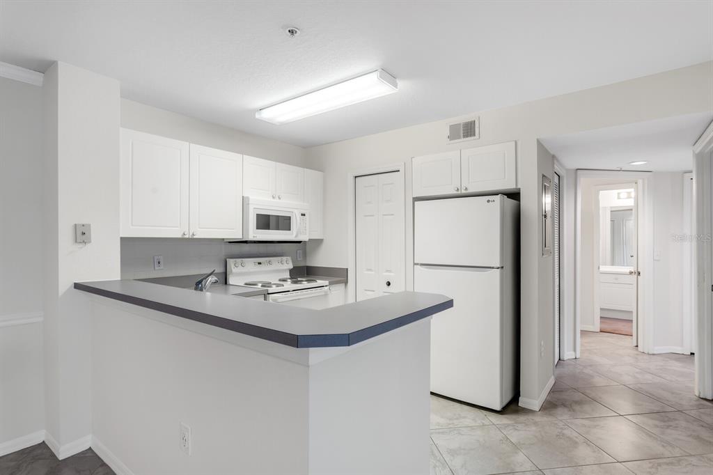 A kitchen features white cabinets, white appliances, and a gray countertop breakfast bar — 18108 PEREGRINES PERCH PLACE UNIT 7110, LUTZ, FL
