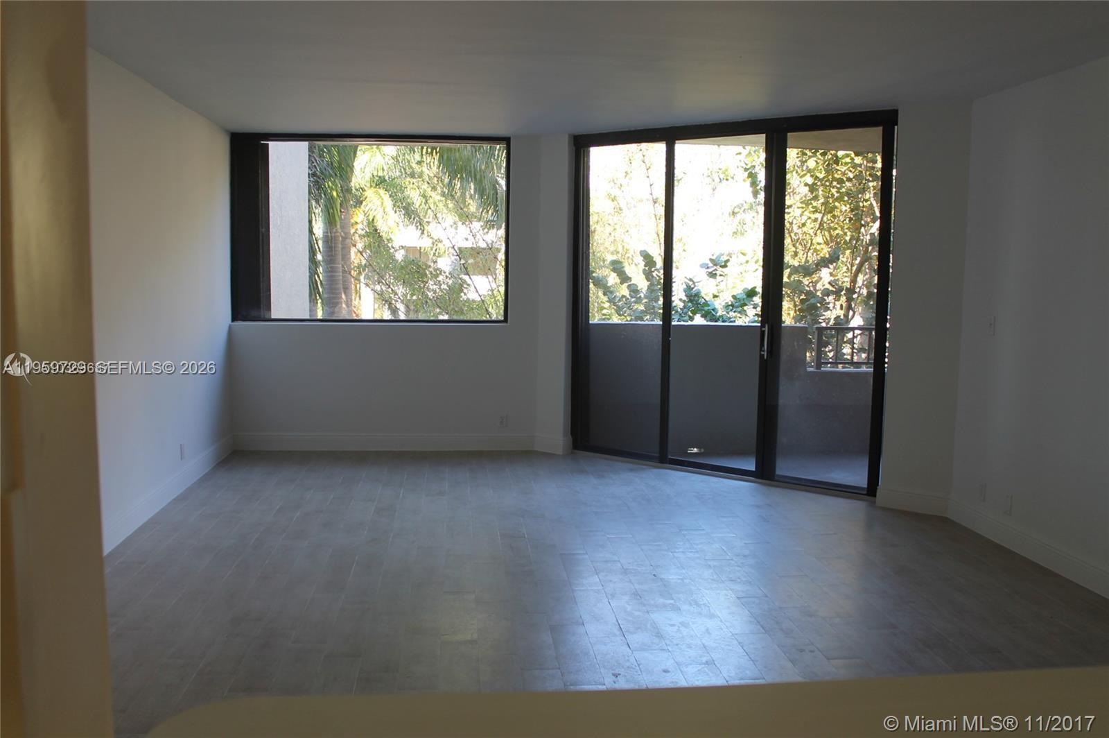 An empty living room features light wood-look flooring, white walls, and a sliding glass balcony door — 181 Crandon Blvd # 308, Key Biscayne FL 33149, KEY BISCAYNE, FL