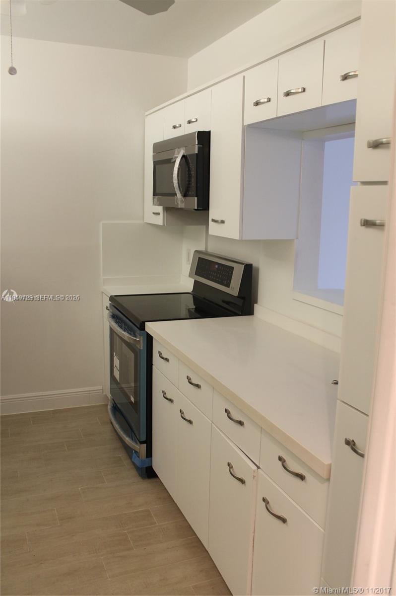 A white kitchen features a stainless steel stove, microwave, and light-colored tile flooring — 181 Crandon Blvd # 308, Key Biscayne FL 33149, KEY BISCAYNE, FL