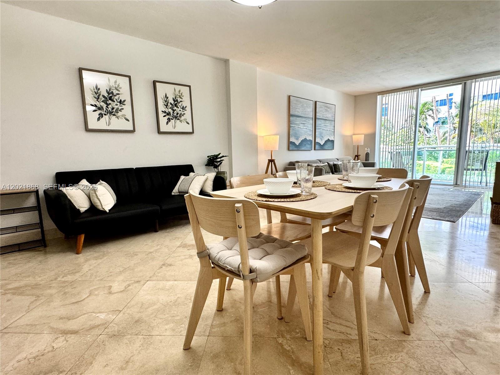 A dining area with a light wood table and chairs sits beside a black sofa — 3001 S Ocean Dr # 119, Hollywood FL 33019, HOLLYWOOD, FL